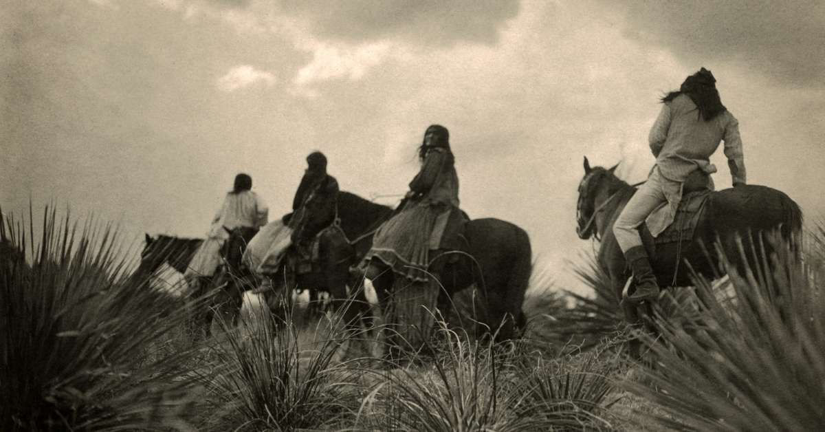 Indians on horses riding in the mountains.