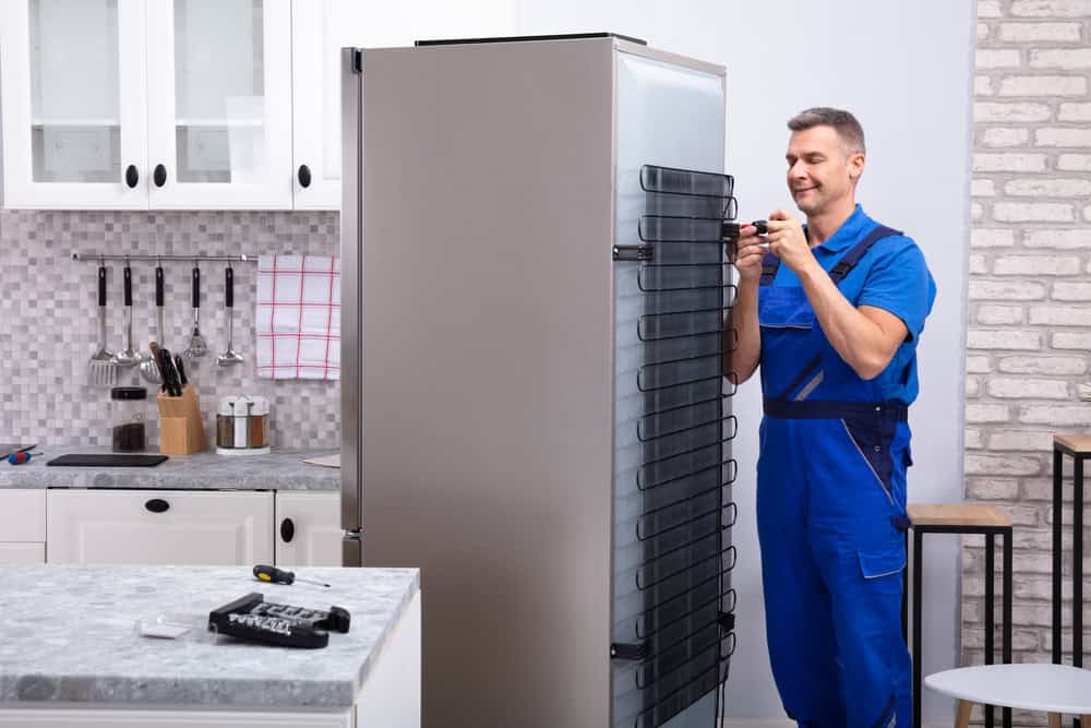 A man cleaning the coils of a refrigerator in a home in Scottsdale AZ