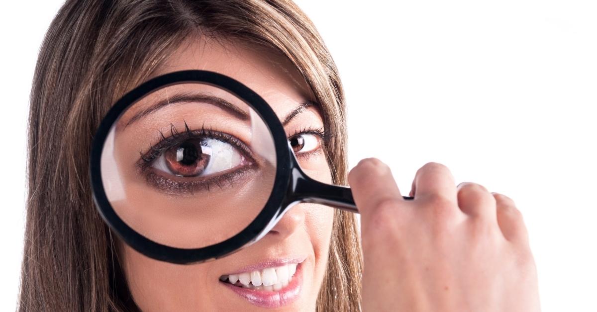 A woman holding a magnifying glass up in front of one of her eyes