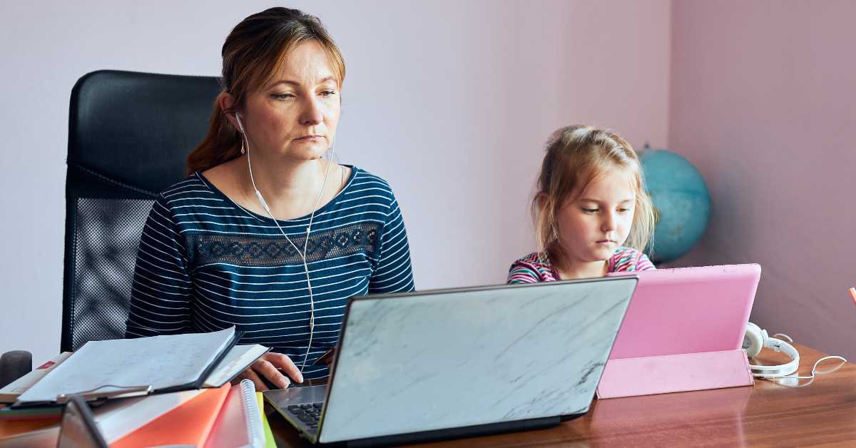 A mother working remotely on her laptop with her daughter by her side with a pink laptop in their Scottsdale home office.