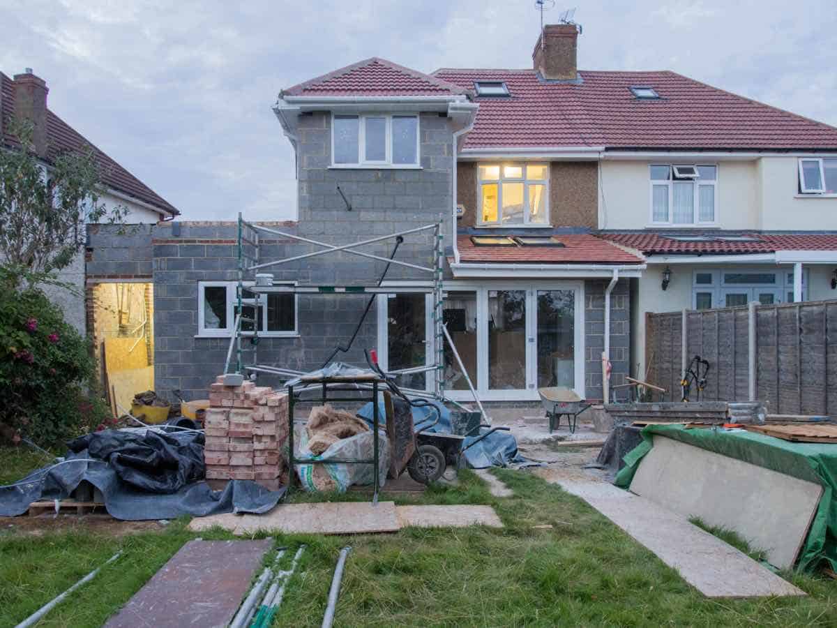 Residential home addition under construction with scaffolding and building materials in the backyard.