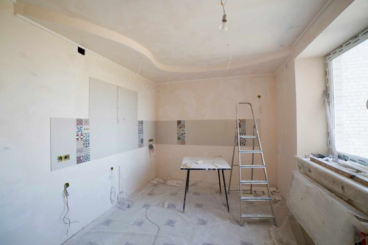 Interior room under renovation with ladder, wiring, tile work, and unfinished surfaces.