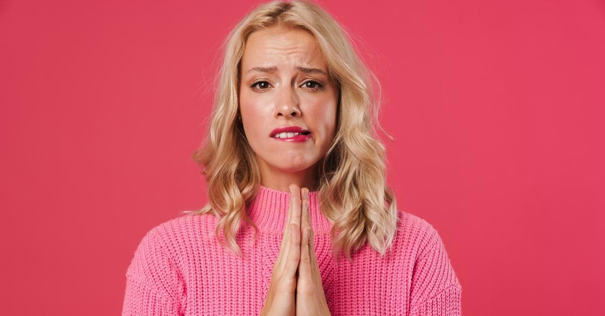 A Scottsdale home buyer in a pink sweater with a pink background biting her lip and praying