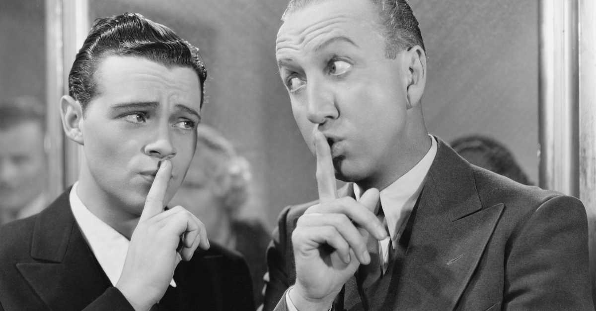 A black and white photo of 2 men in an old movie both using their finger to say 